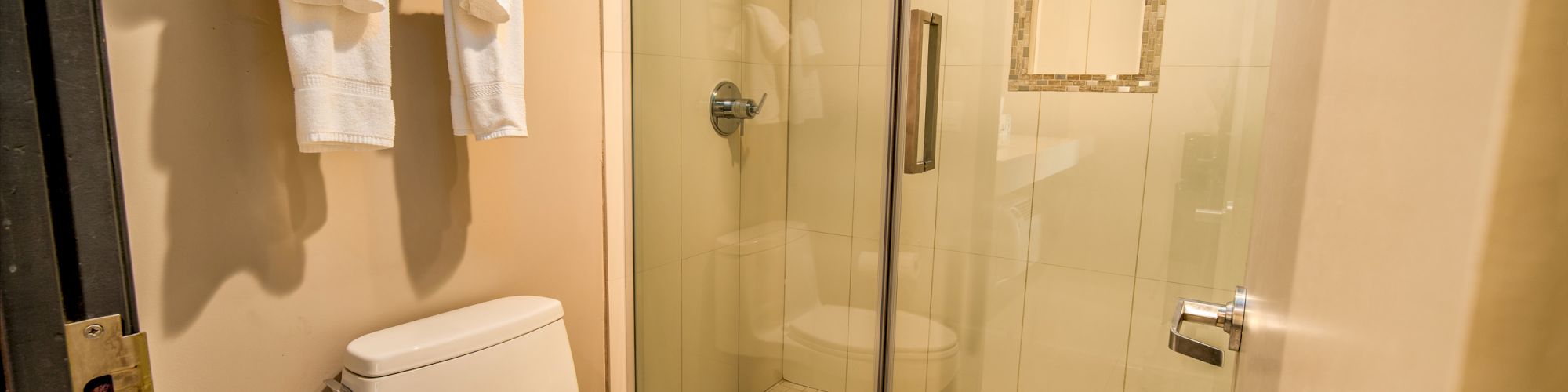 A bathroom with a toilet, glass-enclosed shower, and towel rack holding folded and hanging towels.