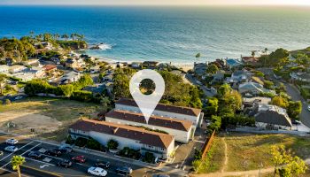 An aerial view of a coastal neighborhood with a location pin marking a specific building, near the beach and ocean.