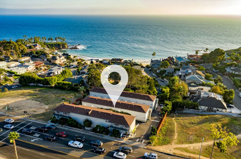 An aerial view of a coastal neighborhood with a location pin marking a specific building, near the beach and ocean.