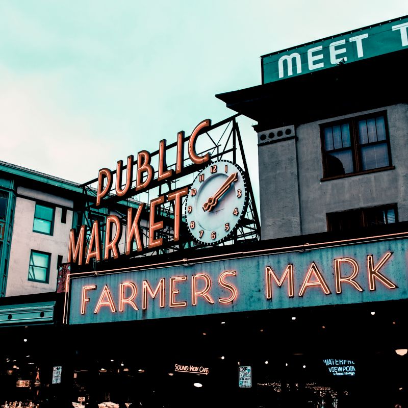 An outdoor scene depicts a "Public Market" sign with a clock above, and a "Farmers Market" sign below, with building facades and a partial sign visible.