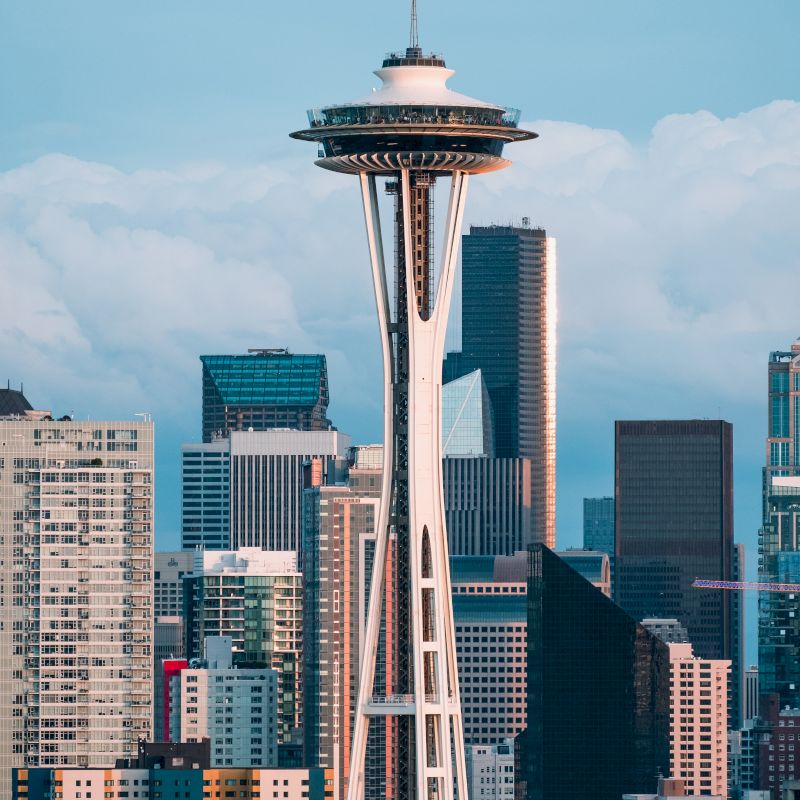 The image shows the Space Needle in Seattle, Washington, with the city skyline and skyscrapers in the background under a clear sky.