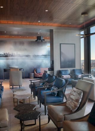 A modern lounge with comfortable seating, large windows with a scenic view, and elegant decor, featuring a mural of a city skyline.
