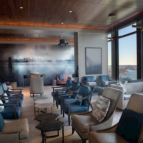 This image shows a modern lounge area with comfortable seating, large windows offering ocean views, and several tables and chairs.