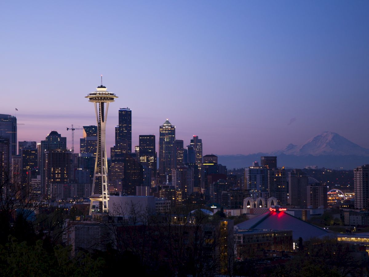 This image shows the Seattle skyline at dusk, featuring the Space Needle prominently, with Mount Rainier in the background.