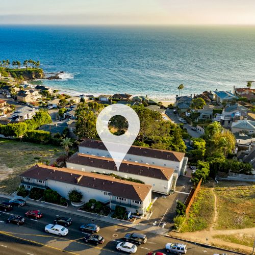 An aerial view of coastal houses and buildings next to the ocean, with a location pin marking a specific building.